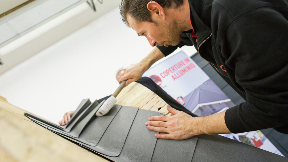 Ein Teilnehmer der PREFA Academy befestigt sorgfältig Aluminium-Dachziegel auf einem Modell. Er verwendet einen Gummihammer, um die Aluminiumplatten präzise zu positionieren. 