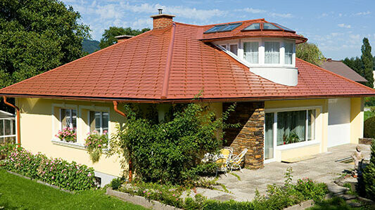 Einfamilienhaus mit Walmdach und Gaube, gedeckt mit PREFA Aluminiumschindeln in ziegelrot.