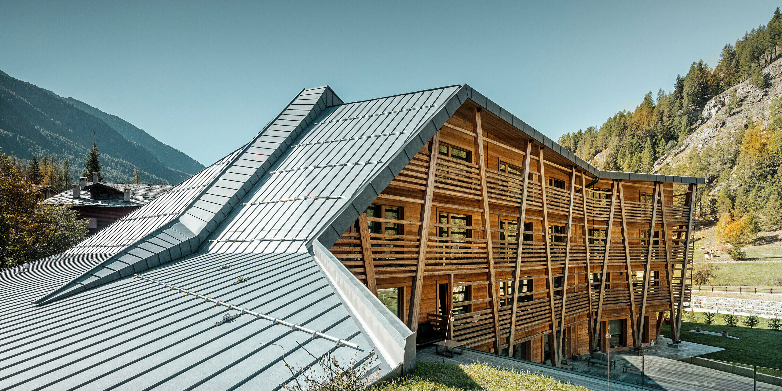 Das Hotel 'Au Charmant Petit Lac' in Champoluc zeigt eine einzigartige architektonische Harmonie, bei der das PREFALZ Dachsystem in P.10 Steingrau gekonnt mit der holzverkleideten Struktur des Gebäudes verschmilzt. Die dynamische Dachgestaltung mit ihren klaren Linien und Falzen fügt sich nahtlos in die umliegende Alpenlandschaft ein und bietet einen modernen Kontrast zur traditionellen Holzbauweise. Diese Kombination aus modernen und natürlichen Materialien spiegelt das Engagement des Hotels für umweltbewusstes Design und Nachhaltigkeit wider.