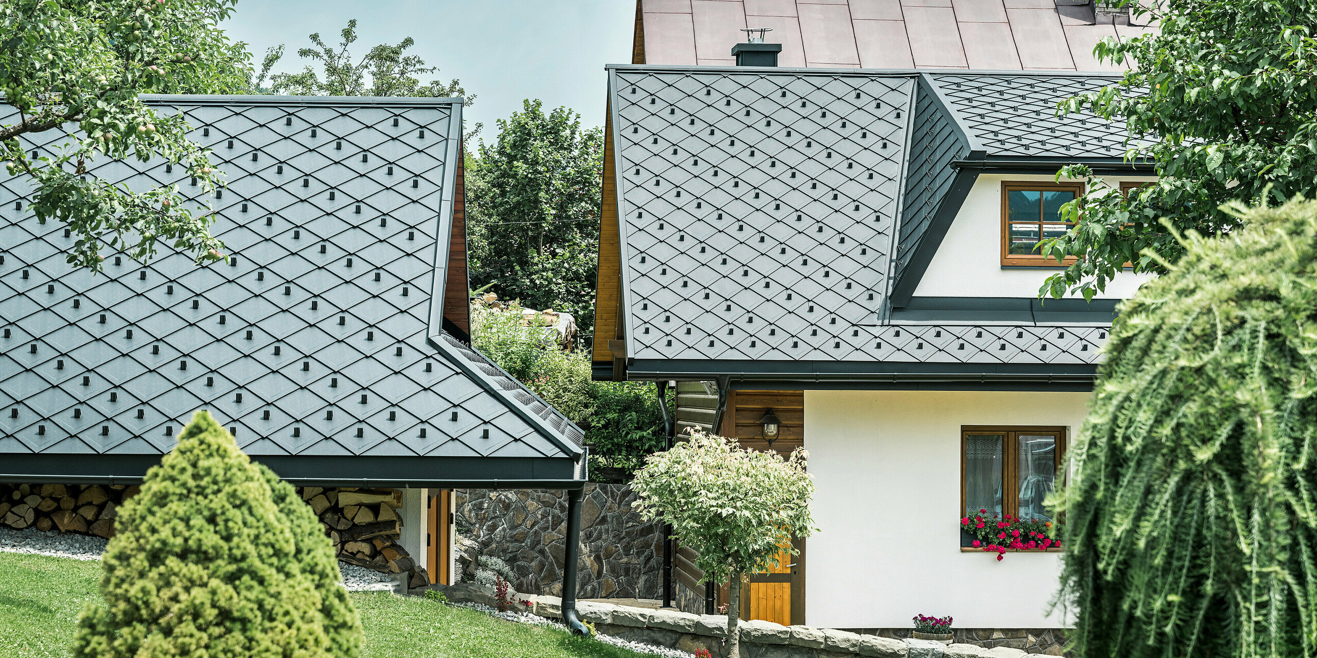 Detaillierte Ansicht der Dächer eines Einfamilienhauses und Zubaus in Stara Bystrica, Slowakei, eingedeckt mit PREFA Dachrauten 29 × 29 in P.10 Schwarz. Die Dachlandschaft zeigt eine elegante Schuppenoptik, die durch robuste Aluminiumrauten erreicht wird. Die klare Linienführung und die harmonische Gestaltung der Dächer fügen sich perfekt in die Umgebung ein und betonen das moderne und stilvolle Erscheinungsbild des Gebäudes.