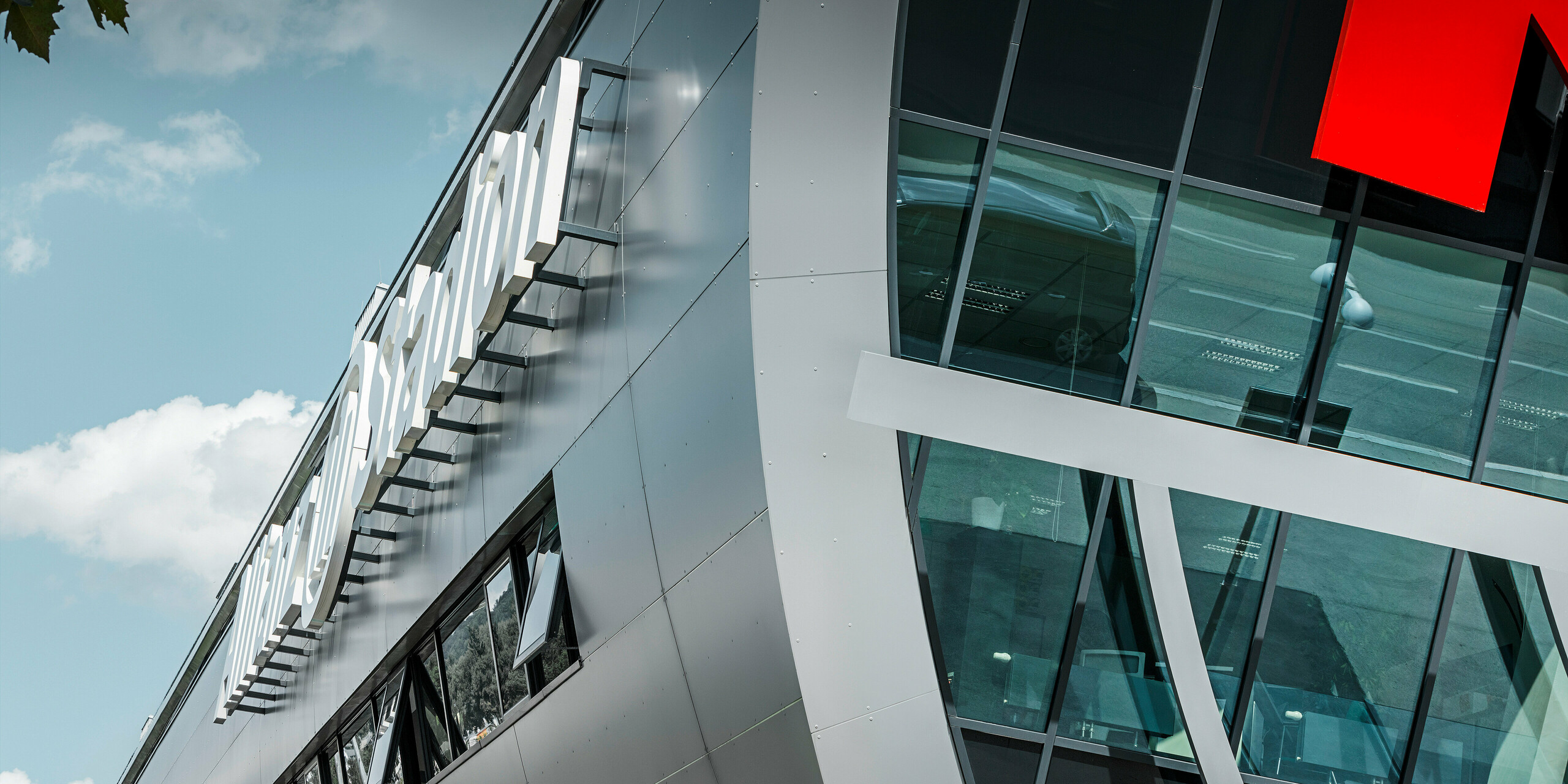 Detailaufnahme der Fassadenverkleidung des Allianz Stadions, der Heimstätte des SK Rapid Wien. Der Fokus des Bildes richtet sich auf die glänzende Fassade aus PREFA Aluminium Verbundplatten in Silbermetallic. Am Bildrand sind der Name des Bauwerks „Allianz Stadion“ sowie die großen Glasflächen und ein Ansatz des leuchtend roten Logos von Rapid Wien zu erkennen.