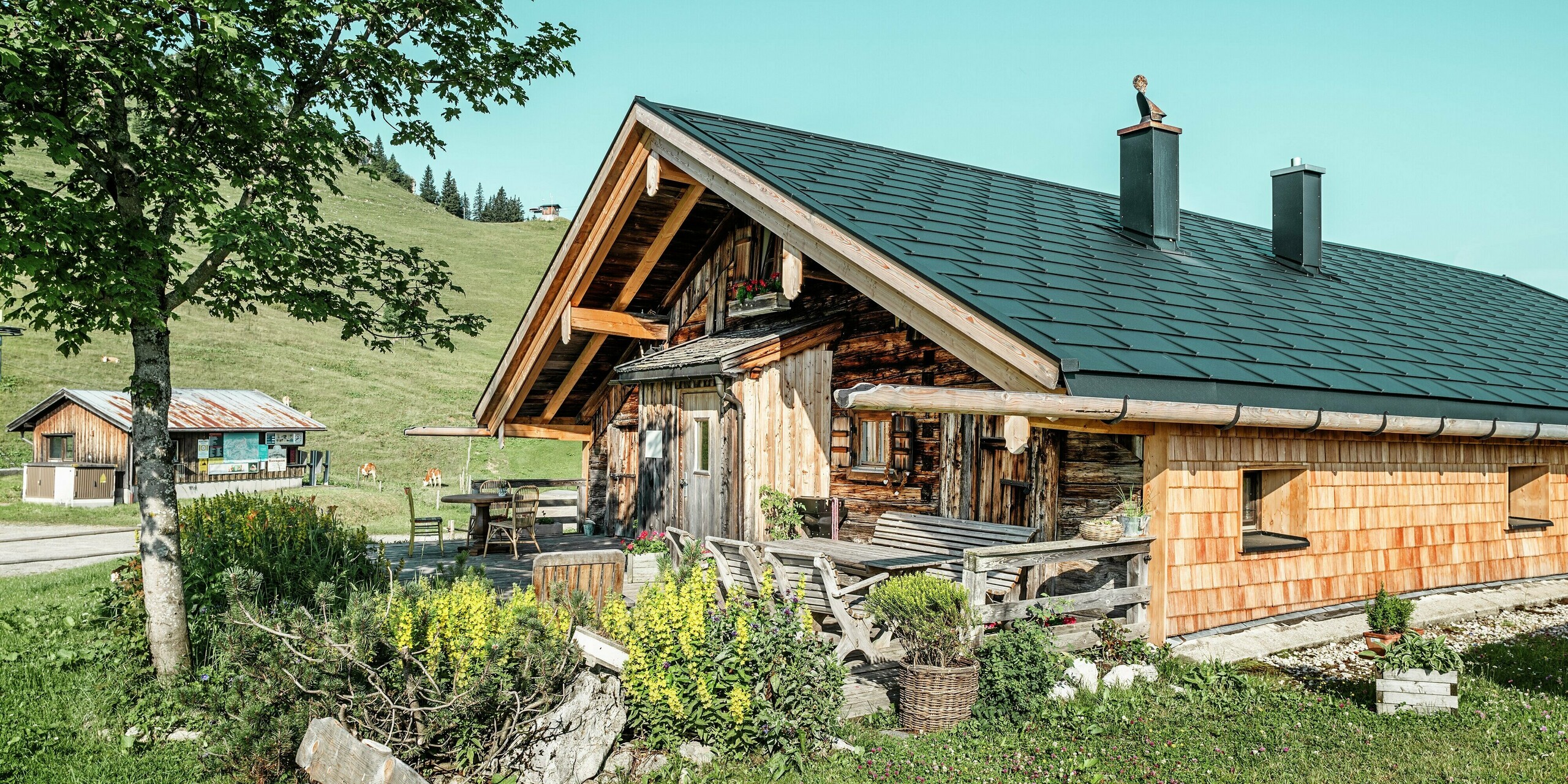 Traditionelle Holzhütte auf der Walleralm in Bayrischzell mit hochwertigem PREFA Dach- und Dachentwässerungssystem. Im Zuge einer Dachsanierung wurden langlebige PREFA Dachplatten R.16 in der Farbe P.10 Schwarz sowie innovative PREFA Solardachplatten verlegt. Das rustikale Holzdesign der Hütte harmoniert mit der einzigartigen Dachentwässerung aus Holz und Aluminium. Durch die Dachsanierung verbindet die Hütte energieeffiziente Solartechnik mit dem bewährten Schutz der robusten Aluminiumprodukte von PREFA.