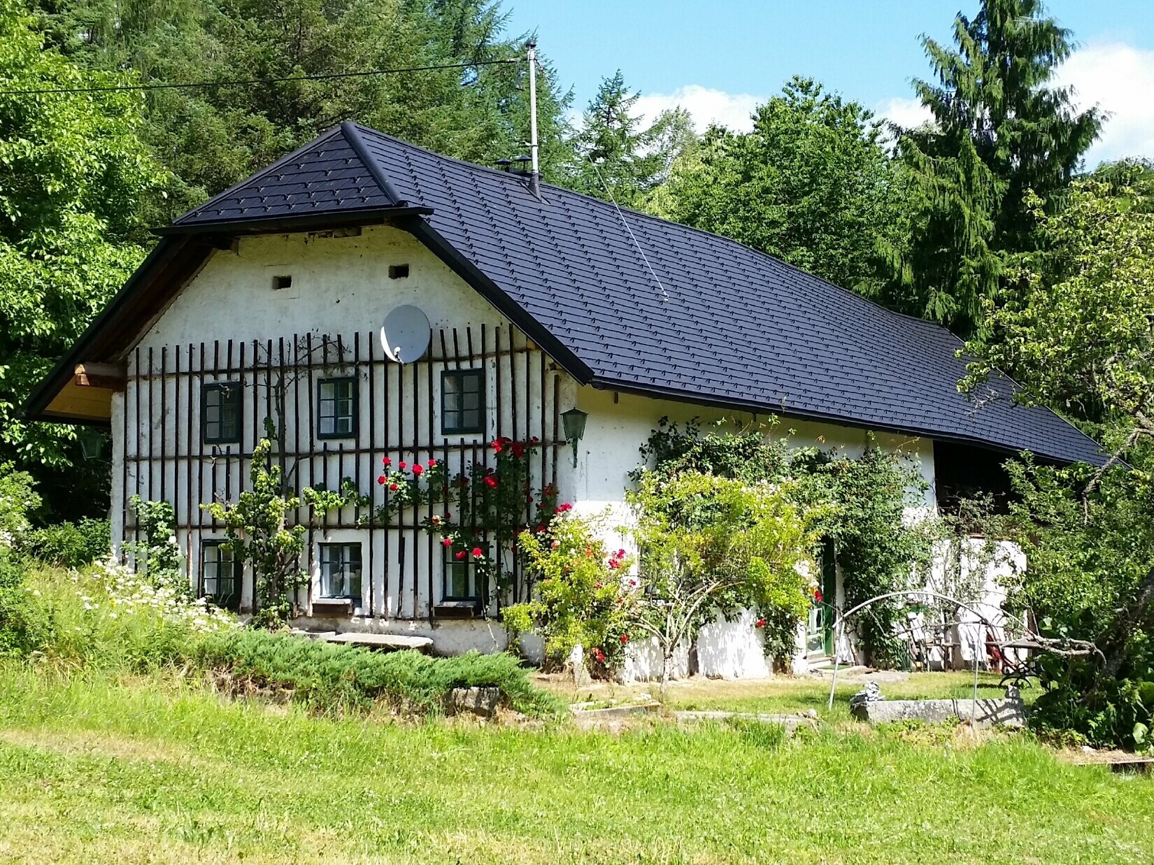 A háttérben a mezei ház látható. A 400 éves ház, melynek tetőjét P.10 színű PREFA tetőzsindelyekkel újították fel. 