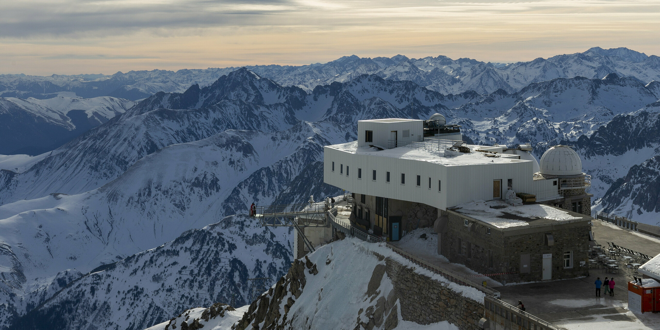 Das Midi-Pyrénées-Observatorium, umfassend saniert und erweitert, thront auf einem verschneiten Berggipfel. Die Fassade wurde mit PREFALZ in der Farbe P.10 Reinweiß gestaltet, was sich aufgrund der extremen Hochgebirgsbedingungen als ideal erwies. Die Wetterbeständigkeit, Korrosionsbeständigkeit und Wartungsarmut von PREFALZ, kombiniert mit der leichten Transportierbarkeit per Hubschrauber, machten es zur optimalen Wahl. Die Bauarbeiten, die aufgrund der anspruchsvollen Bedingungen nur im Sommer durchgeführt werden konnten, dauerten über drei Jahre. Im Hintergrund erstrecken sich die majestätischen, schneebedeckten Pyrenäen.Die Sonne scheint durch die weißen Wolken und verleiht dem Bild Helligkeit.