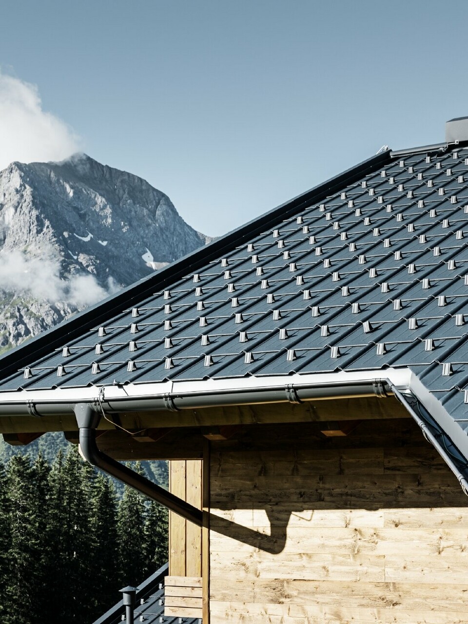 Faház a hegyekben, a tetőt PREFA Classic elem borítja antracit színben PREFA ereszcsatornával és fa homlokzattal