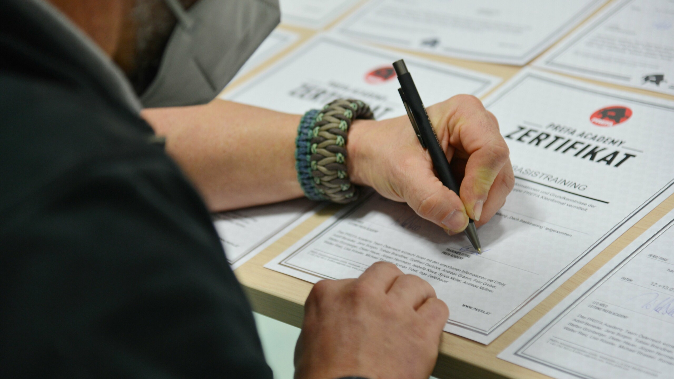 Ein Kursleiter der PREFA Academy unterschreibt ein Zertifikat nach Abschluss eines Kurses aus. Mehrere Zertifikate liegen auf dem Tisch bereit. Diese Szene zeigt den Abschluss eines Trainingsprogramms und die Ausstellung von Teilnahmezertifikaten in der PREFA Academy.