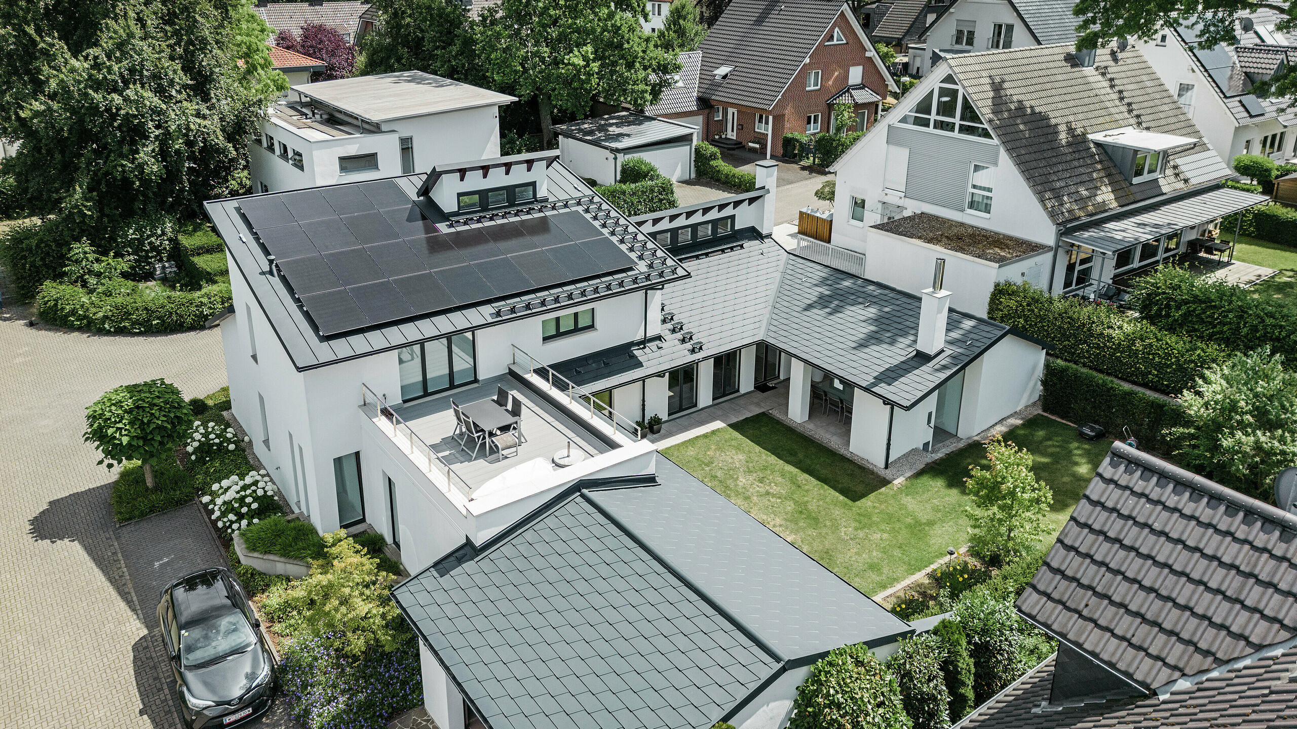 Madártávlatból egy dortmundi családi ház kiemelkedő tetőtájképe PREFA tetőzsindellyel DS.19 és PREFALZ P.10 antracit színben, valamint egy nagyméretű PV-rendszerrel.
